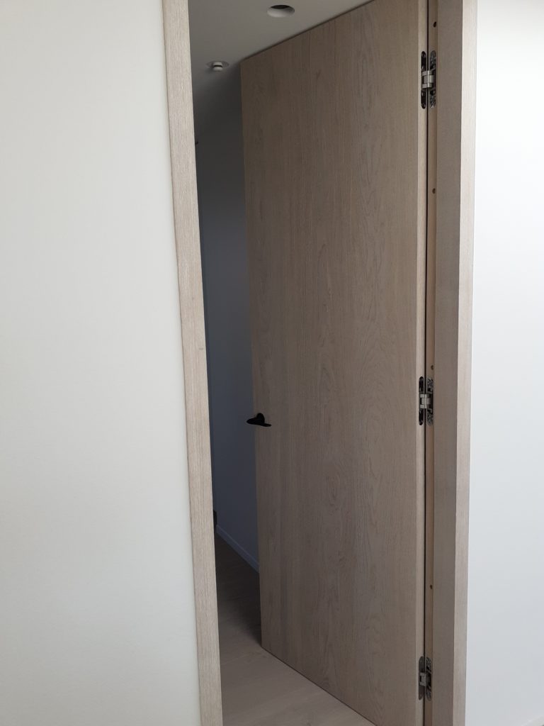 Modernistisk villa med minimalistisk stil fik specialdesignede høje, uindfattede døre i børstet egefinér  fra Madsen Vinduer og Døre. Her ses hvordan dørbladet flugter med gulv og loft. Her ses hvordan dørbladet flugter med gulv og loft.